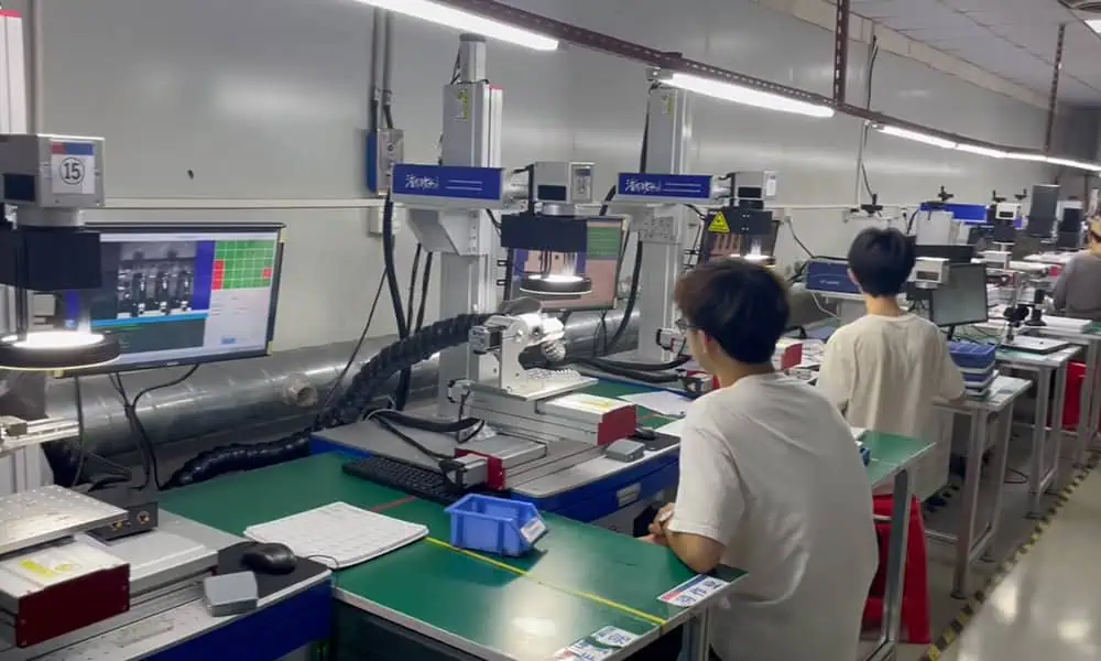 Sistemas personalizados de marcação a laser com eixo XYZ dispostos em várias estações de trabalho de produção, com cabeças de laser verticais, estágios de posicionamento, monitores de computador e operadores