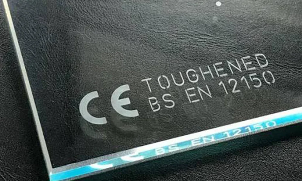 Laser-marked tempered glass sample showing permanent compliance text and symbols