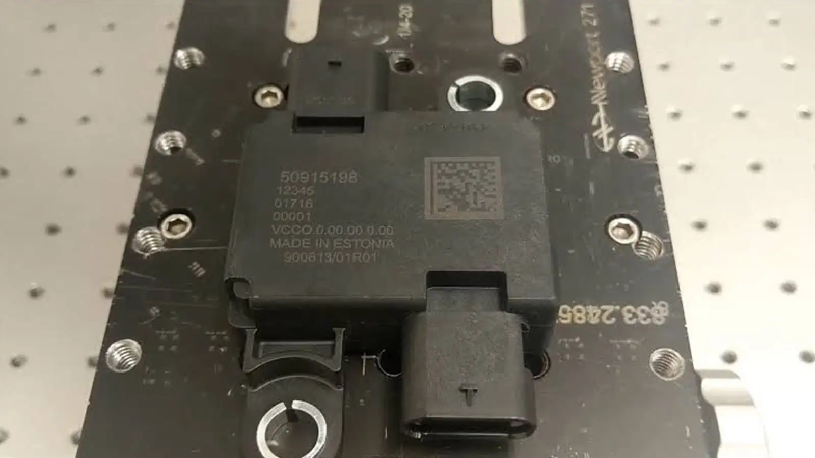 Automotive connector component held in a fixture with laser-marked text and Data Matrix code